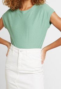 Top texturizado color verde menta con mangas cortas, combinado con una falda de mezclilla blanca de tiro alto con una abertura frontal y cierre de botones.