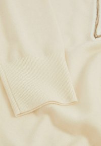 Cremfarbener gestrickter Pulloverstoff mit gerippten Bündchen, glatter Textur und sanftem Fall, der ein dezentes kontrastierendes Ausschnittdetail aufweist.