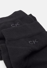 Calze nere a coste realizzate in tessuto morbido, con un piccolo logo "ck" grigio sul risvolto. Senza motivi distintivi o accenti aggiuntivi.
