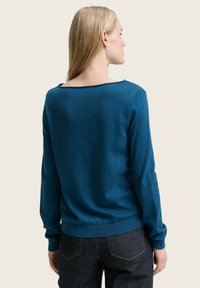Teal gebreide trui met lange mouwen en een wijde halslijn, voorzien van geribbelde manchetten en zoom. Gestyled met donkere spijkerbroeken.