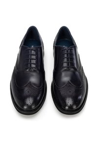 Czarne skórzane eleganckie buty męskie z ozdobnymi perforacjami typu brogue i zamkniętym sznurowaniem, ustawione obok siebie na białym tle.