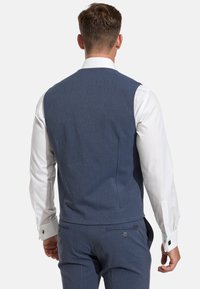 Gilet en laine bleu avec une texture lisse, présentant une coupe ajustée, des détails de couture au dos, associé à une chemise blanche à manches longues.