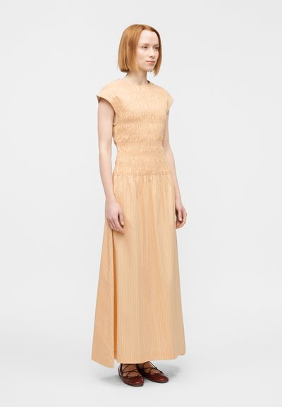 Φόρεμα μέχρι το γόνατο σε ροδακινί απόχρωση με κορσέ με σφηκοφωλιά και ρέον φούστα. Ριγωτή υφή και κοντά μανίκια. Φορεμένο με καφέ, δετά σανδάλια.