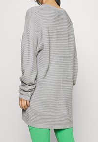Maglione lavorato a maglia grigio chiaro oversize con costine orizzontali, spalle scese e maniche a polsini, abbinato a leggings verdi in tessuto texturizzato.