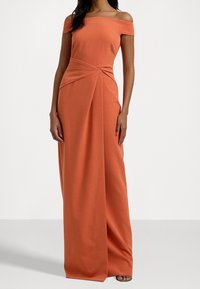 Axelklänning i lång orange färg med en figurnära överdel, vriden detalj vid midjan och en flödande kjol i mjukt tyg.