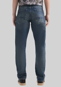 Jeans in denim blu scuro con taglio dritto, cuciture visibili e due tasche posteriori, abbinati a sneakers nere.