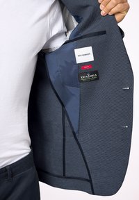 Slimowana granatowa marynarka z teksturowanej tkaniny, z kontrastowym wewnętrznym podszewką i czarnymi akcentami, z metkami i kieszenią w środku.