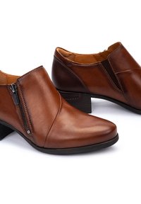 Bottines en cuir marron avec un bout pointu, fermeture éclair latérale et accents élastiques, dotées d'un petit talon empilé et d'une texture lisse.