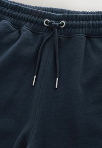 Pantaloni sportivi blu scuro con vita elastica e coulisse regolabile con punte in metallo annodate.