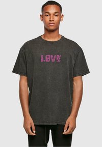 Zwarte oversized katoenen t-shirt met een ronde hals, voorzien van een paarse "LOVE" grafische print op de voorkant, textuurstof en een ontspannen pasvorm.