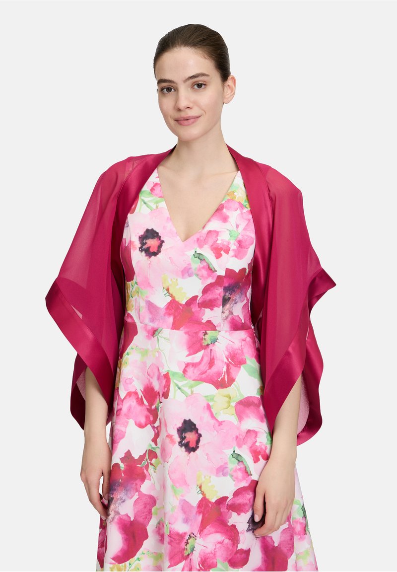 Ein transparenter magentafarbener Schal liegt über einem Kleid mit Blumenmuster, das große rosa und grüne Blumen auf hellem Hintergrund zeigt. V-Ausschnitt-Design.