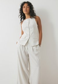 White pinstriped suit featuring a sleeveless, fitted vest with buttons and pockets, paired with wide-leg trousers for a coordinated look.