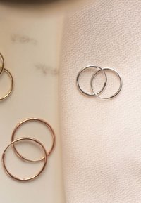 Zilveren en roségouden oorringen tentoongesteld op een neutrale stoffen achtergrond, die ronde vormen en zachte metallic afwerkingen laten zien.