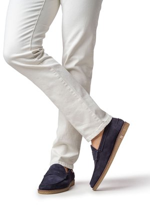Chaussures à enfiler en daim bleu marine avec une finition texturée et une semelle en caoutchouc marron clair, associées à un pantalon de couleur crème.
