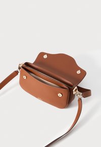 Brown leather crossbody bag with a scalloped top, gold hardware, two compartments, and a long adjustable strap. Smooth texture and minimalist design.