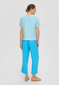 Top de manga corta azul claro combinado con pantalones sueltos de color azul brillante y sandalias planas, visto desde atrás sobre un fondo neutro.