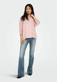 Lyserød skjorte med knapper og afslappet pasform samt puffærmer, parret med lyseblå flared jeans og sorte spidse hæle.