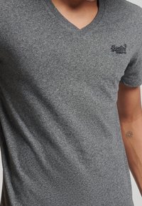 T-shirt grigio a scollo a V realizzato in tessuto testurizzato, con un logo ricamato sottile sulla parte sinistra del petto. Maniche corte e vestibilità casual.