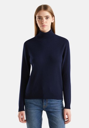 Pull à col roulé marine fabriqué en tissu doux et texturé. Il présente des manches longues et une coupe ajustée, associé à un jean en denim.