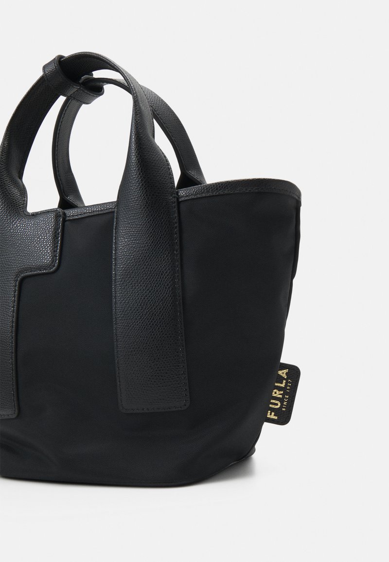 Schwarze Tragetasche mit strukturierten Lederakzenten und glattem Stoff. Sie hat kurze Griffe und ein goldenes Logo-Tag. Modernes, strukturiertes Design.