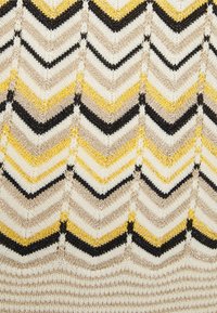 Strickstoff mit einem Zickzackmuster in Schwarz, Gelb und Beige, das verschiedene Streifen aus weichen, strukturierten Garnen zeigt.