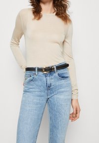 Beige dlouhý rukáv top vyrobený z lehkého materiálu, spárovaný se světle modrými džíny, zdobený černým páskem se zlatou sponou.