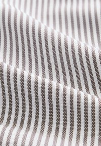 Stoff mit abwechselnden braunen und weißen Streifen, gewebt mit einer strukturierten Oberfläche, die ein dezentes Muster über die Fläche erzeugt.