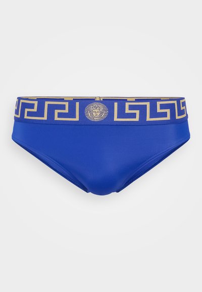 Blaue Schwimmslips mit glatter Oberfläche, ausgestattet mit einem goldfarbenen, gemusterten Bund und einem Medusa-Emblem in der Mitte.