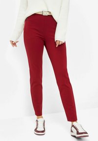 Red fitted pants made of smooth material, paired with white and burgundy sneakers. Sweater is cream with a textured knit design.