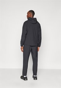 Sort letvægtsjakke med hætte, parret med matchende bukser. Glat stof, minimalistisk design og en afslappet pasform. Mørke sko fuldender outfittet.