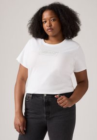 White cotton t-shirt with short sleeves, featuring a silver embroidered "LEVI'S" logo on the chest, paired with black denim jeans.