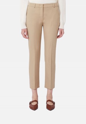 Pantaloni beige su misura alla caviglia indossati con scarpe Mary Jane marroni e appuntite e una maglia bianca a maniche lunghe.