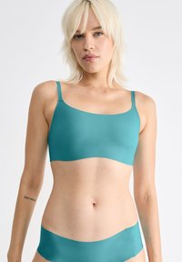 Turkos sömlös bralette med tunna axelremmar och matchande lågt skurna trosor, tillverkad av mjukt, elastiskt tyg, utan synlig hårdvara eller mönster.