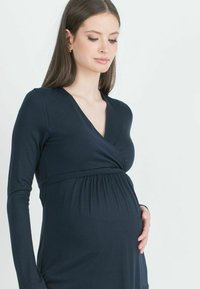 Tummansininen äitiysmekko pitkillä hihoilla, V-pääntie ja kerätty vyötärö, valmistettu pehmeästä, joustavasta kankaasta. Silkkinen rakenne.