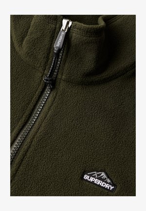 Zielony polarowy sweter z wysokim kołnierzem, z suwakiem na pół, czarnym uchwytem zamka i małym czarnym haftowanym logo.