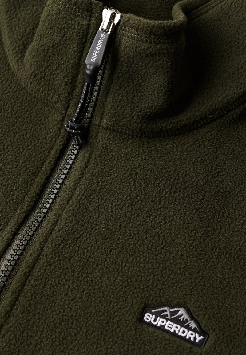 Groene fleece pullover met een hoge kraag, voorzien van een half-rits sluiting, zwarte rits trekker en een klein zwart geborduurd logo.