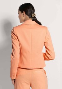 Perzikkleurige blazer met een getailleerde pasvorm, notch-lapels en drie knopen aan de manchetten. Effen textuur met minimale stikseldetails aan de achterkant.