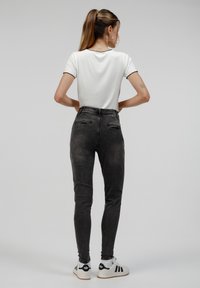 Jeans de tiro alto en gris oscuro con corte ajustado, combinados con una blusa blanca con bordes negros en forma de onda. Zapatillas blancas visibles.