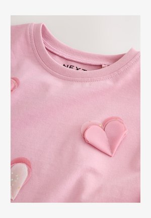 Lyserød bomuld T-shirt med rund hals, forsynet med lagdelte, teksturerede lyserøde hjerteapplikationer på forsiden. Glat stof med en blød finish.