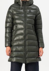 Abrigo acolchado verde con acabado brillante, que cuenta con capucha, cremallera frontal y bolsillos laterales. El diseño incluye secciones acolchadas para aislamiento.