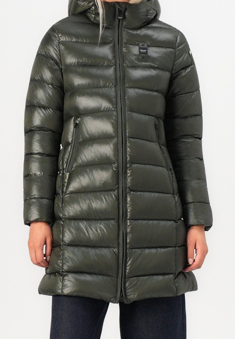 Abrigo acolchado verde con acabado brillante, que cuenta con capucha, cremallera frontal y bolsillos laterales. El diseño incluye secciones acolchadas para aislamiento.