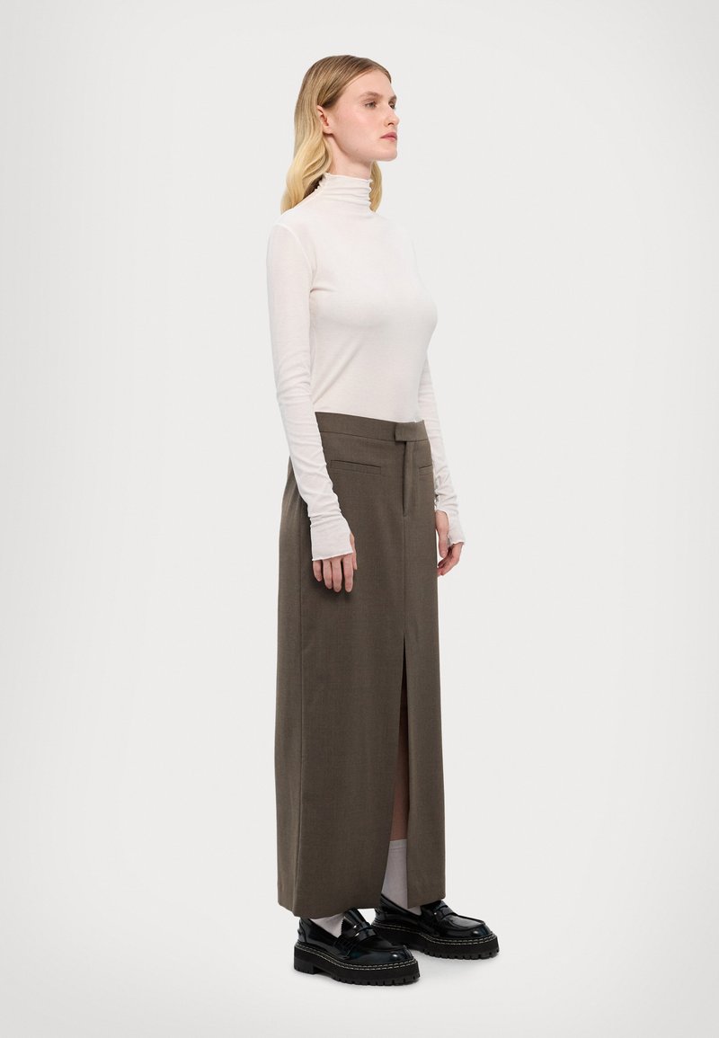 Hosszú ujjú, világos bézs garbó, amely egy sötét olívazöld, magas derekú szoknyával van párosítva, elől hasítékkal. Fekete platform cipők fűzős kivitelben.