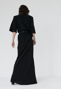 Czarna, oversize'owa bluzka z szerokimi rękawami, zestawiona z długą czarną spódnicą. Gładka faktura materiału, z paskiem w talii do modelowania sylwetki.