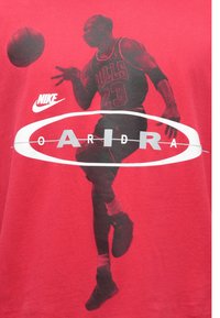 Κόκκινο βαμβακερό t-shirt με μεγάλο μαύρο γραφικό ενός παίκτη μπάσκετ, με το κείμενο «BULLS 23» και λευκό οβάλ λογότυπο.