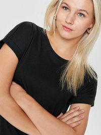 Schwarzes Kurzarm-T-Shirt mit Rundhalsausschnitt. Glattes Baumwollmaterial. Das Modell hat blonde Haare in einem natürlichen Look und steht mit verschränkten Armen.