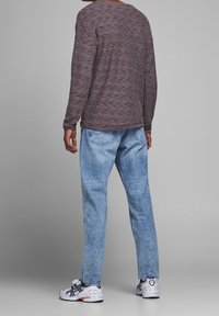 Pull à manches longues texturé couleur bordeaux, jean bleu clair à jambes droites, et chaussures de sport blanches avec des accents noirs et orange.