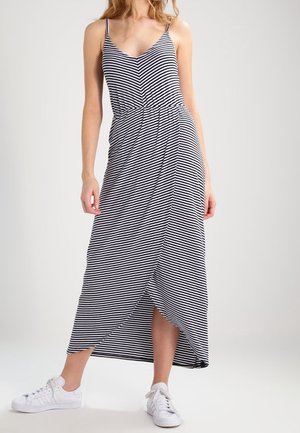 Sukienka maxi w czarno-białe paski, z cienkimi ramiączkami, taliowana w pasie i z rozcięciem po bokach, zestawiona z białymi trampkami.