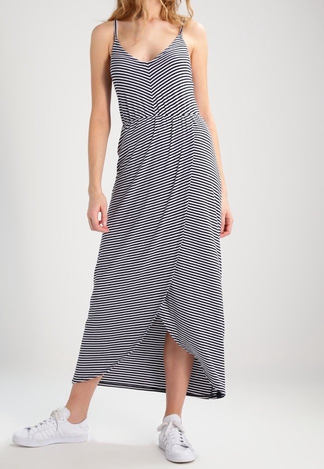 Robe maxi rayée en noir et blanc avec bretelles spaghetti, taille cintrée et fente latérale, associée à des baskets blanches.