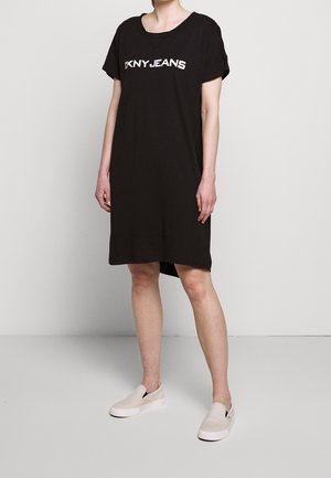 Czarna bawełniana sukienka o luźnym kroju, z krótkimi rękawami i okrągłym dekoltem. Na przodzie znajduje się biały napis „DKNYJEANS”.
