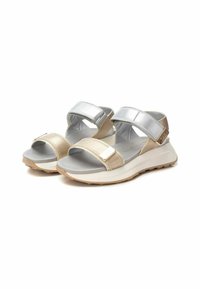 Las sandalias metálicas en plata y beige presentan dos correas ajustables, una plantilla gris acolchada y una suela texturizada para un mejor agarre.